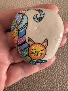 Hand holding white stone painted with colorful patterned cat illustration
