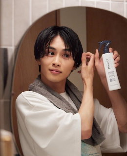 Young man in white robe holding a white bottle near a round mirror in a bathroom