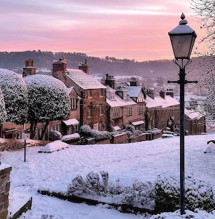 Snow-covered village cottages with street lamp at sunset under pink sky