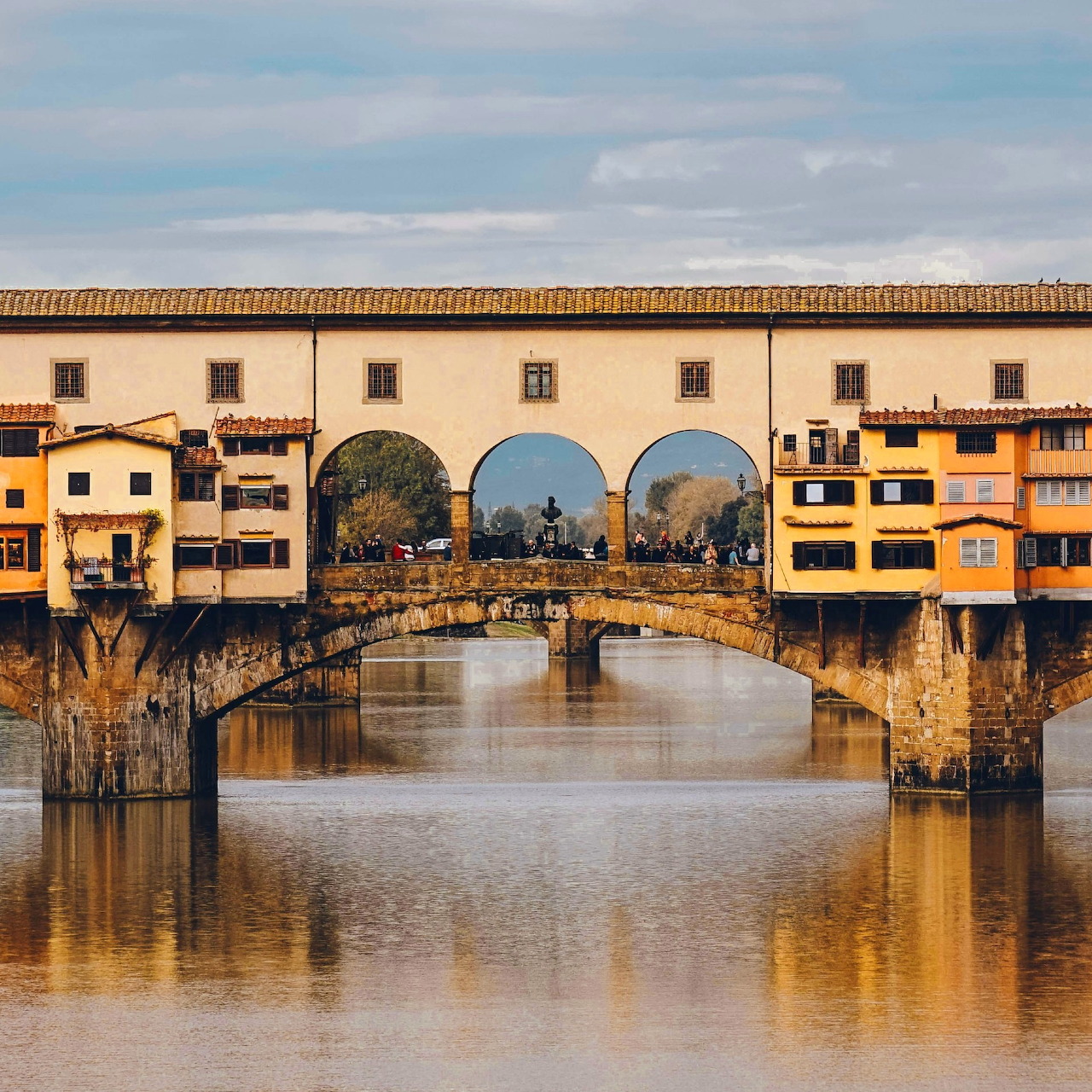 Ponte Vecchio bridge with golden buildings and arches reflected in the Arno River, Florence