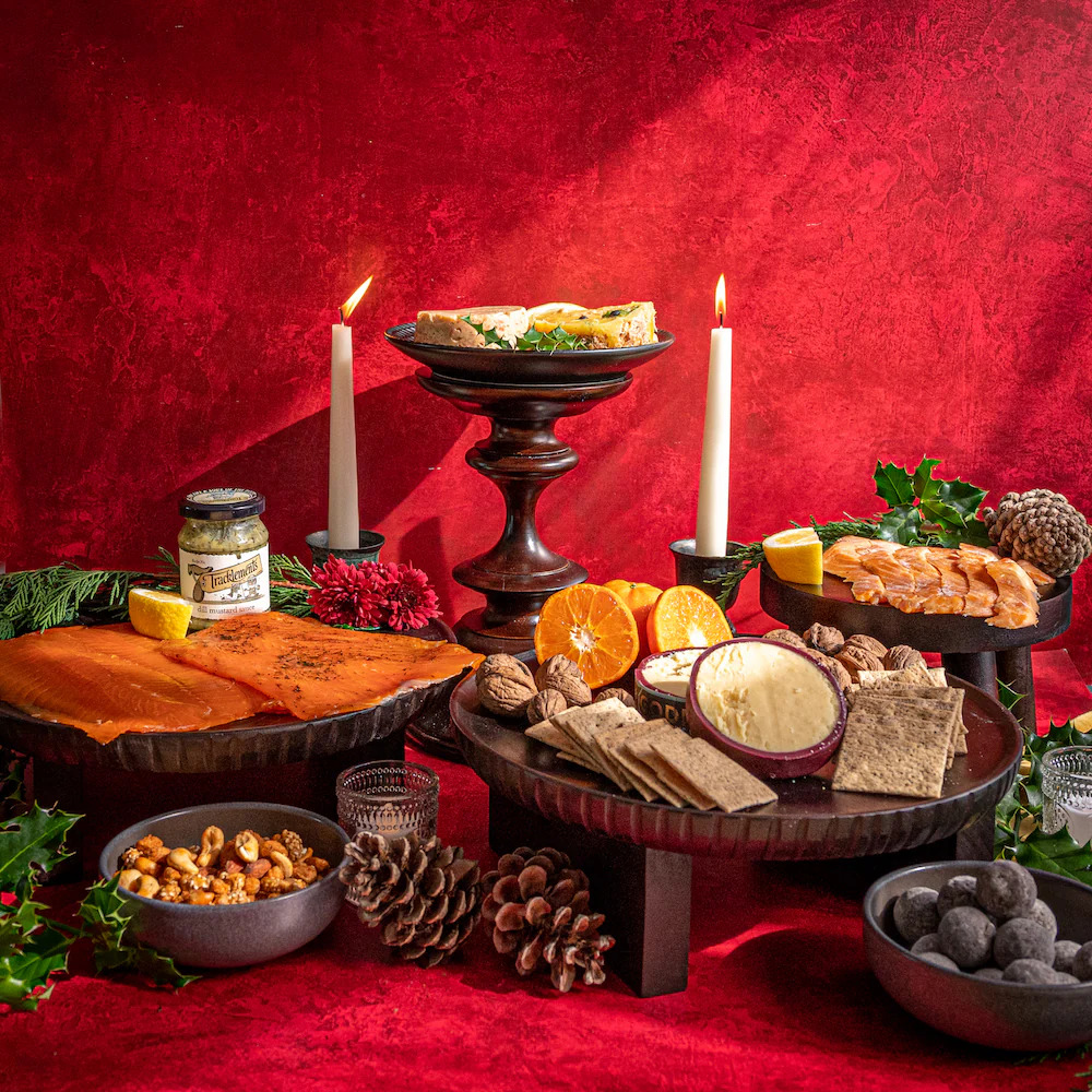 Festive table with candles, cheese, salmon, fruits, nuts, and pine cones on red background