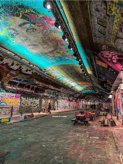 Graffiti-covered tunnel with turquoise ceiling art and people walking through an urban underground archway