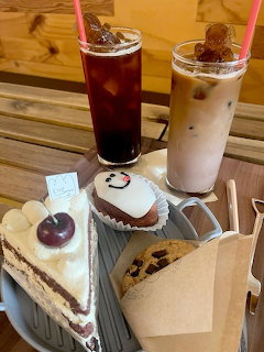 Cafe tray with iced coffee,iced tea, cherry cake slice, cupcake with smiley face, and chocolate chip cookie