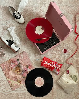 Flatlay with pink record player, red vinyl, sadle shoes, Sweethearts candy box, and dried flowers