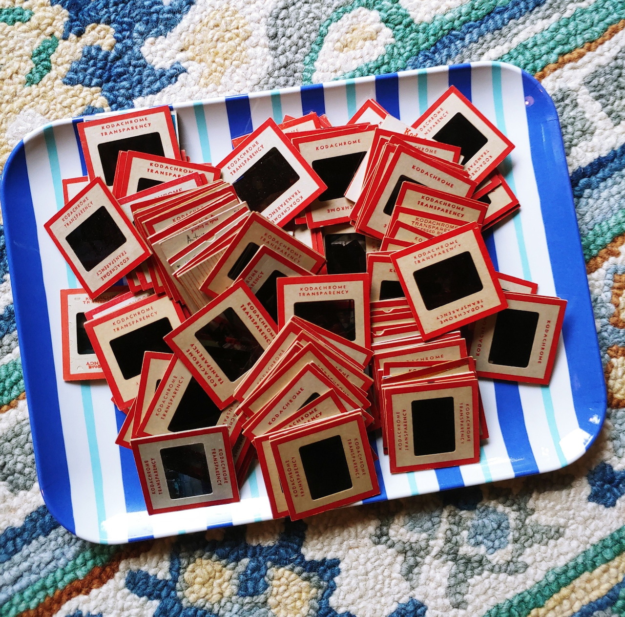 Pile of vintage 35mm photo slides with red striped frames on a blue and white striped tray