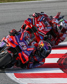 Two MotoGP motorcycles leaning through a corner on a race track with red and white curbing