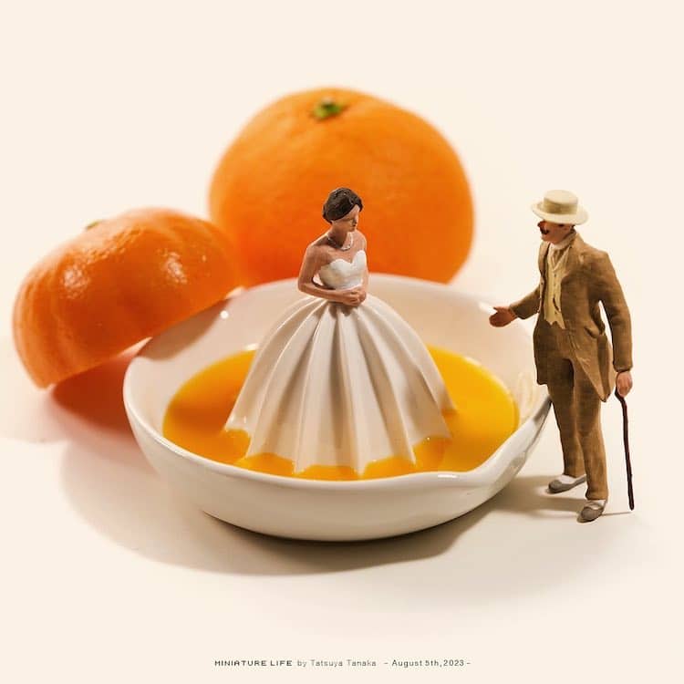 Tiny figurines of elegant couple next to manual orange juicer with whole oranges on white background