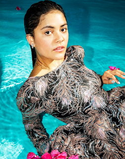 Woman in patterned swimsuit posing in turquoise pool water with pink flowers