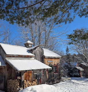 Snow-covered rustic wooden warming hut beside trees under a clear blue winter sky