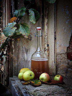 Bottle of homemade apple cider with fresh apples on weathered wood background