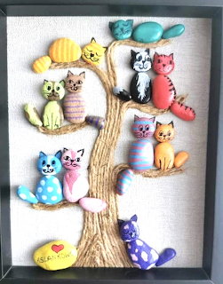 Textile art of colorful stuffed fabric cats sitting on branches of a quilted tree against white background