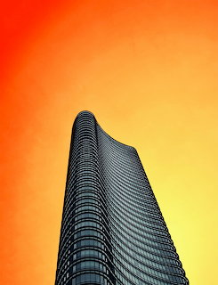 Low-angle view of a curved glass skyscraper against a bright orange sky