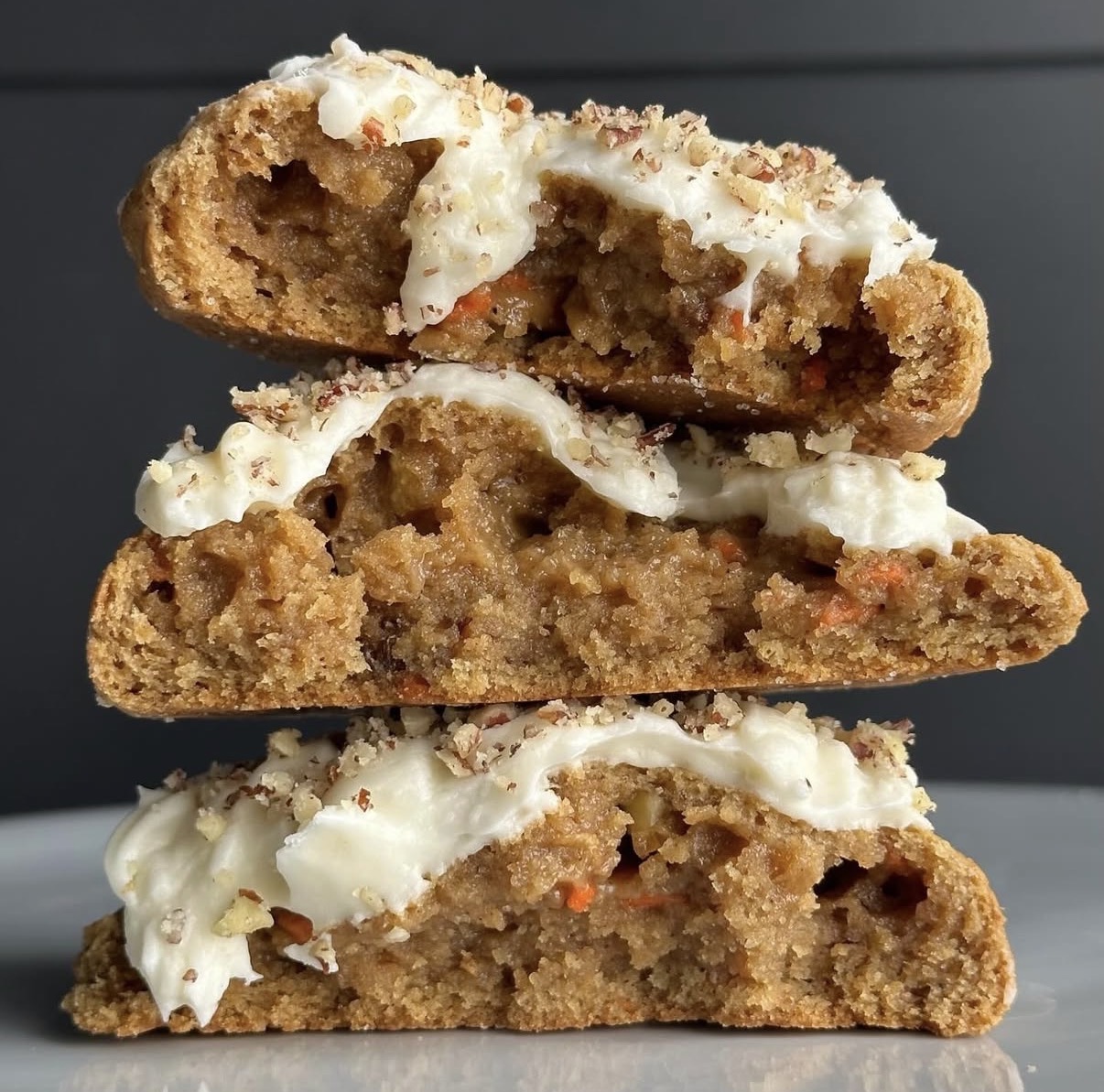 Stack of frosted carrot cookies with creamy white filling on a plate