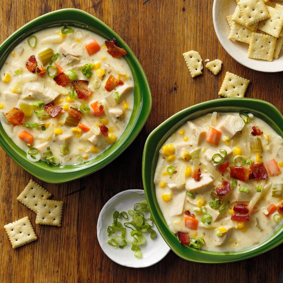 Two bowls of creamy turkey bacon and corn chowder with crackers on a wooden table