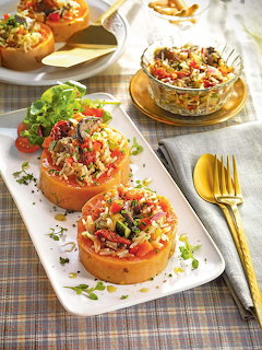 Three stuffed pumpkin halves filled with rice and vegetables on a white rectangular plate with gold utensils