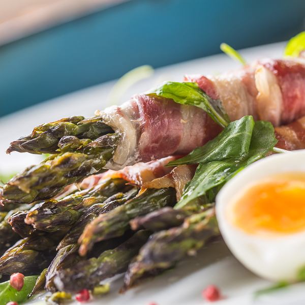 Asparagus spears wrapped in bacon with soft-boiled egg and basil on white plate