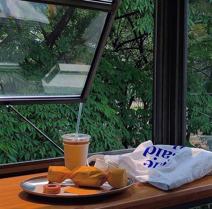 Iced coffee and breakfast plate on wooden table by window with forest view