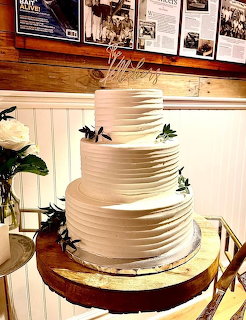 Cream-colored tiered wedding cake with textured icing and topper on a wooden table indoors