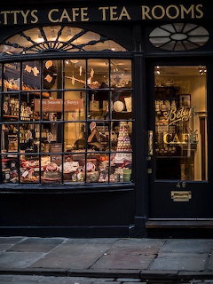 Illuminated storefront of Betty's Cafe Tea Rooms showing display windows filled with teaware and products at night