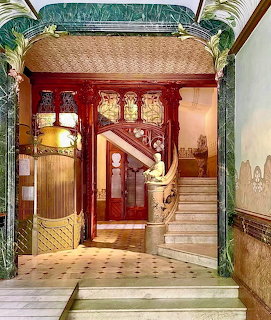 Art Nouveau entrance hall with ornate curved staircase, red walls, stained glass, and decorative tilework