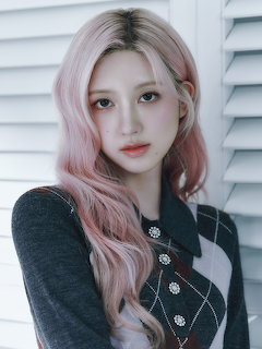Young woman with long pink and blonde wavy hair wearing a dark patterned cardigan