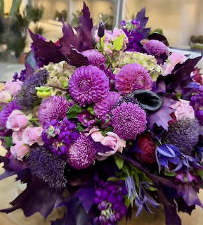 Vibrant purple and pink floral bouquet with dahlias, roses, thistles, and dark purple leaves