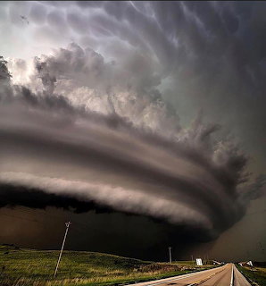 Massive supercell thunderstorm with layered rotating clouds over a highway and green fields