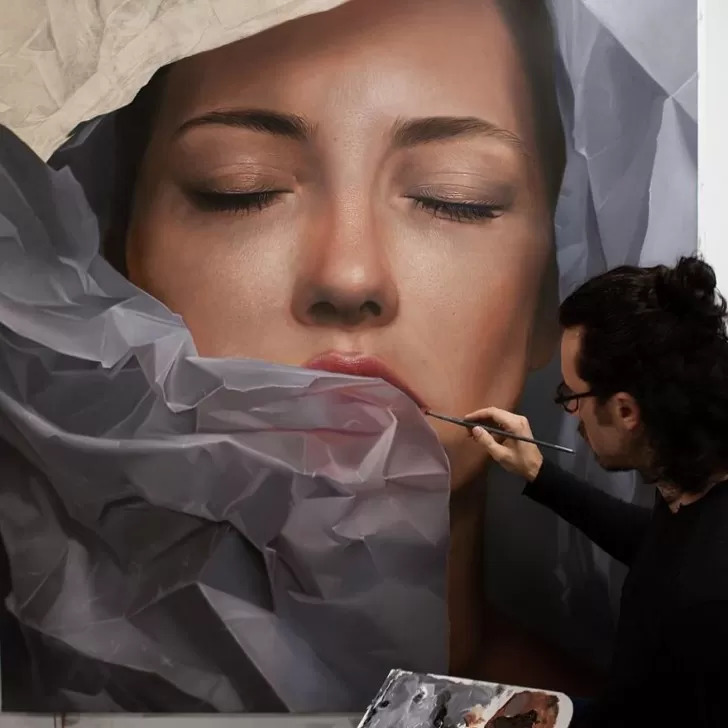 Artist painting a large realistic portrait of a woman's face behind crumpled translucent material