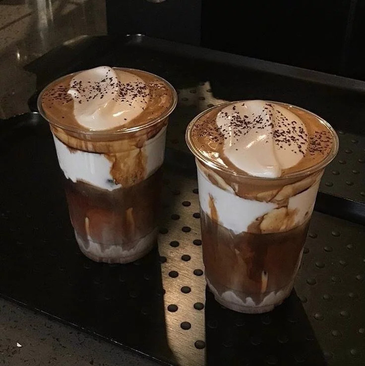 Two iced Einspanner coffee drinks in plastic cups with whipped cream on a dark tray
