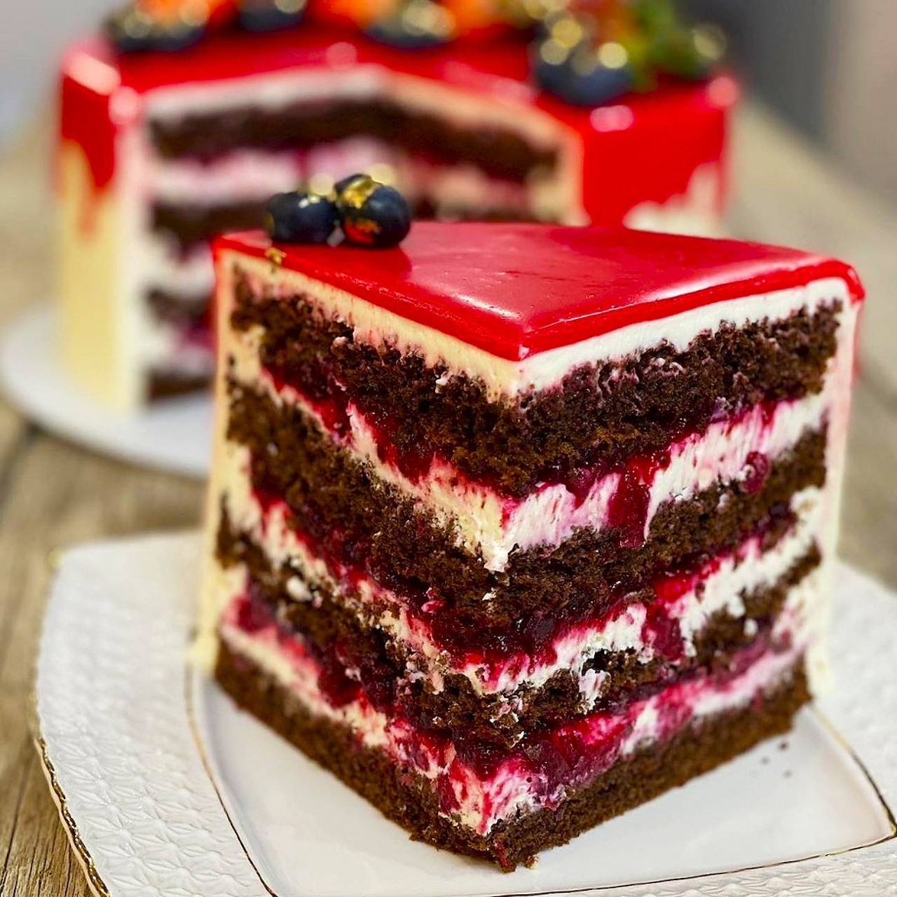 Layered red velvet cake slice with cream filling and red icing on a white plate