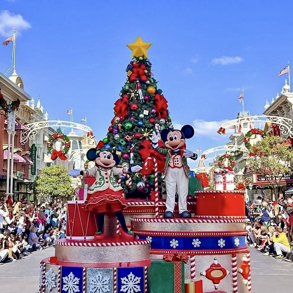Mickey and Minnie Mouse waving from red Christmas parade float with large decorated tree and holiday gifts