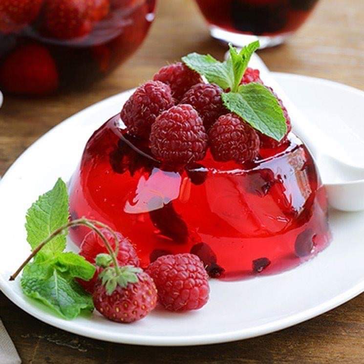 Red jelly dome garnished with raspberries and mint on white plate