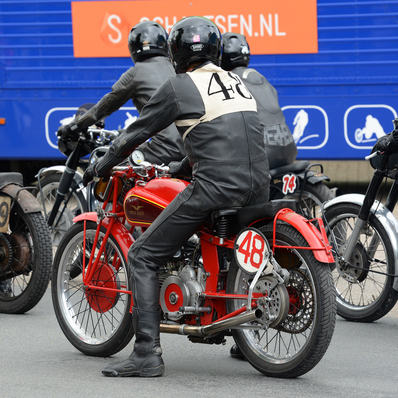 Rider on red vintage Moto Guzzi motorcycle #48 at classic race event with other motorcycles in background