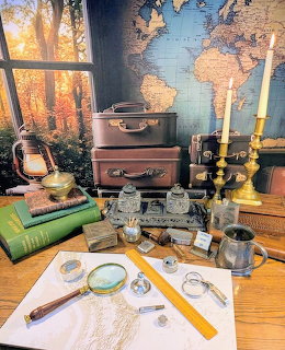 Vintage desk with suitcases, map, magnifying glass, books and travel items by autumn window