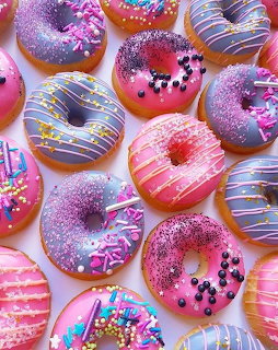 Overhead view of colorful glazed donuts with sprinkles and icing drizzle in pink, purple, and blue tones
