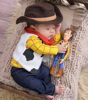 Sleeping baby in cowboy costume holding a Woody doll from Toy Story