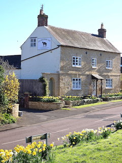Stone cottage beside a road with daffodils and green grass in front