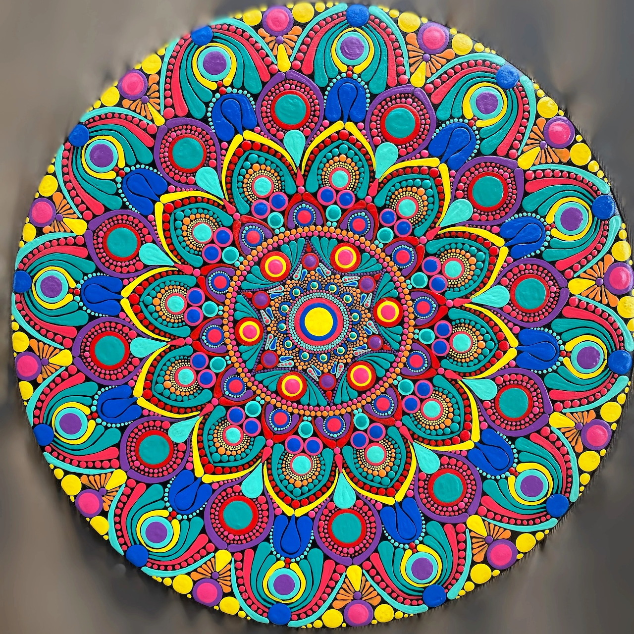 Vibrant circular mandala with intricate dot painting in rainbow colors on gray background