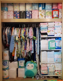 Organized closet with baby clothes, diapers, folded blankets on shelves, and a teal stuffed animal