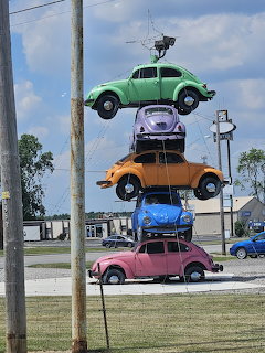 Colorful stack of four VW Beetle cars mounted vertically outdoors by the roadside