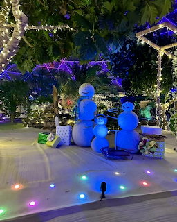 Three glowing blue snowmen under purple-lit greenery with multicolored floor lights in festive indoor display