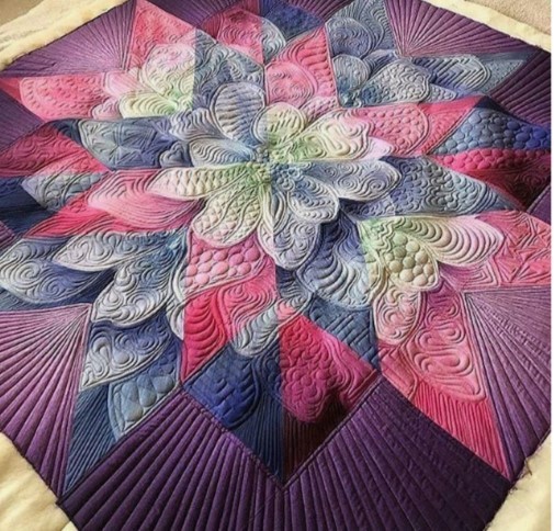 Close-up of ornate quilted star pattern with detailed stitching in pink, purple, blue and cream on dark fabric