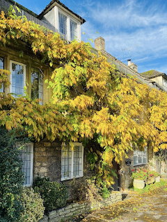 Stone cottage covered in yellow autumn vines under blue sky in Burford, England