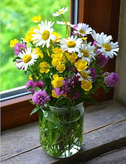 Mixed wildflower bouquet with daisies and yellow flowers in glass vase on windowsill