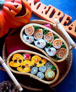 Halloween bento box with kawaii sushi rolls shaped as ghosts and pumpkins next to a jack-o-lantern
