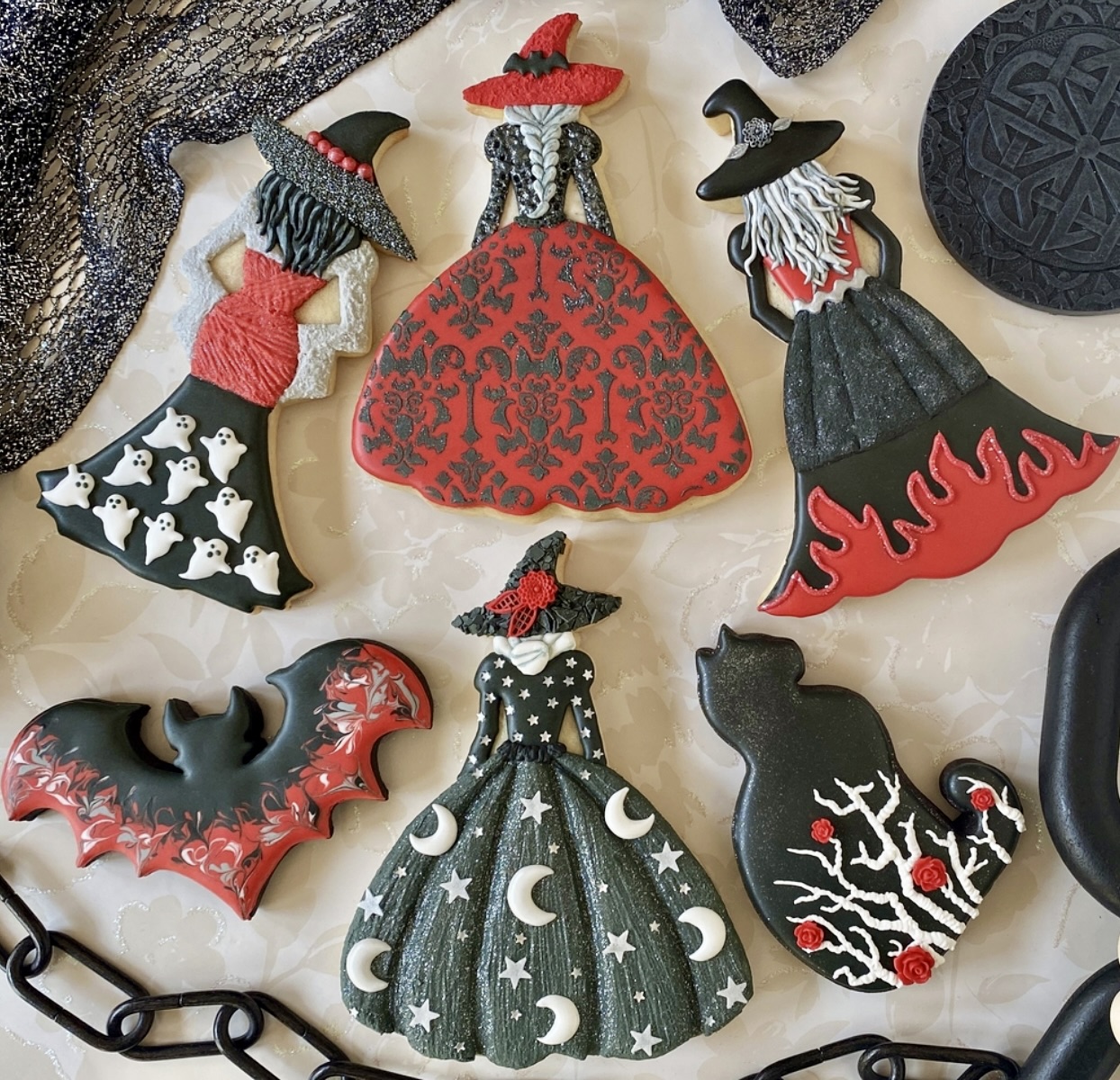 Decorated Halloween cookies shaped as witches with ornate dresses and pointed hats in red, black and white icing