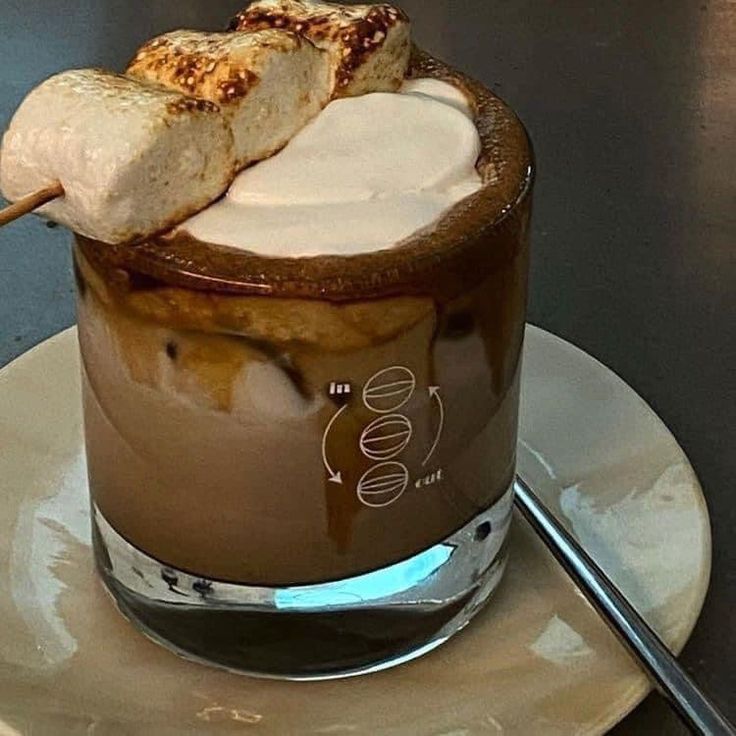 Glass of iced coffee with cream and toasted marshmallows on a saucer beside a spoon