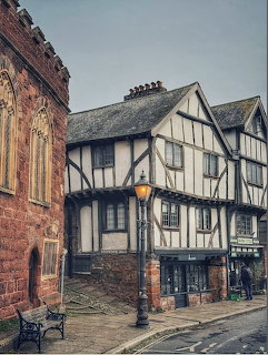 Historic Tudor half-timbered building with black beams and white walls beside a red brick church and glowing street lamp