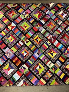 Colorful patchwork quilt with diagonal plaid strips in various bright colors arranged in geometric pattern