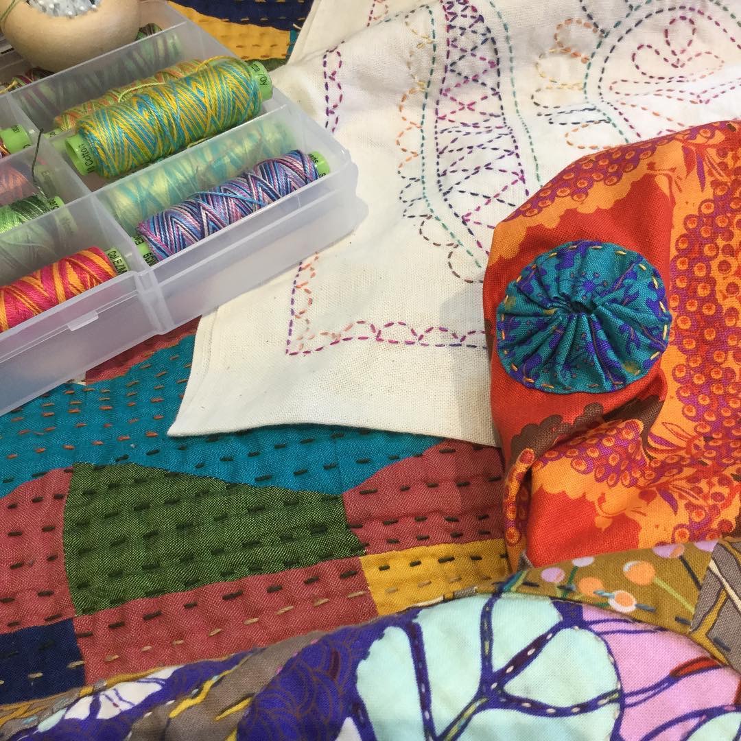 Close-up of colorful quilting fabric, thread spools, and stitched cloth on a patchwork surface